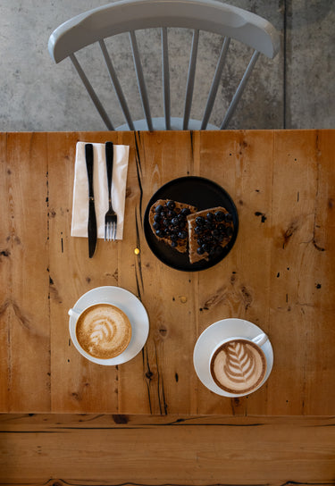 Two cups of coffee with latte art on a wooden table, accompanied by a slice of cake.