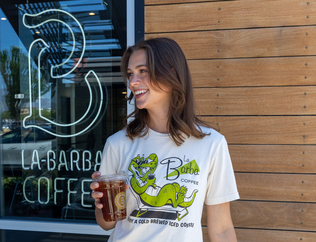 Woman holding a cup of coffee in front of a coffee shop with 'La Barba Coffee' branding.
