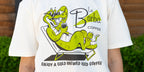 White t-shirt with a green alligator graphic and 'La Barba Coffee' text, worn by a person outdoors.