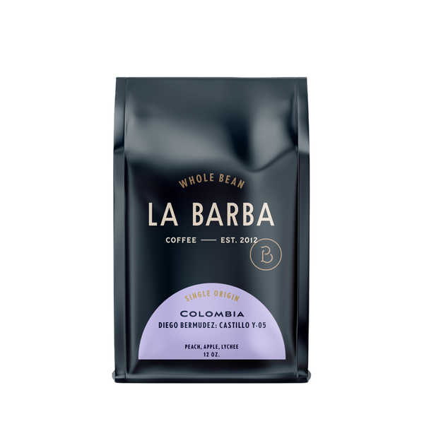 The image features a 12oz bag of La Barba Coffee, specifically their Colombia Diego Bermudez single-origin coffee. The bag is designed with a dark background, prominently displaying the brand name "La Barba" in large, elegant letters. It highlights the coffee's origin, Colombia, along with a description of the flavor profile, including notes of peach, apple, lychee. The design exudes a premium and modern feel with a minimalist, sophisticated look.
