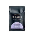 The image features a 12oz bag of La Barba Coffee, specifically their Colombia Sebastian Ramirez red honey bourbon aji. The bag is designed with a dark background, prominently displaying the brand name "La Barba" in large, elegant letters. It highlights the coffee's origin, Colombia, along with a description of the flavor profile, including notes of mint tea, meyer lemon, and honey. The design exudes a premium and modern feel with a minimalist, sophisticated look.