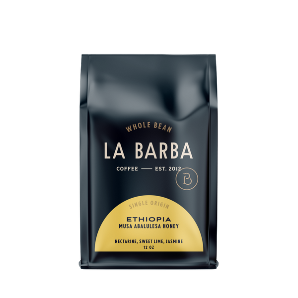 The image features a 12oz bag of La Barba Coffee, specifically their Ethiopia Musa Abalulesa Honey single-origin coffee. The bag is designed with a dark background, prominently displaying the brand name "La Barba" in large, elegant letters. It highlights the coffee's origin, Ethiopia, along with a description of the flavor profile, including notes of nectarine, sweet lime, and jasmine. The design exudes a premium and modern feel with a minimalist, sophisticated look.