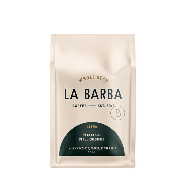 The image features a 12oz bag of La Barba Coffee, specifically their House Blend. The bag is designed with an ivory white background, prominently displaying the brand name "La Barba" in large, elegant letters. It highlights the coffee blend's origins, Peru and Colombia, and includes a description of the flavor profile, including notes of Milk Chocolate, Toffee, and Stone Fruit. The design exudes a premium and modern feel with a minimalist, sophisticated look.