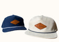 Two hats, one navy and one beige, with a leather patch on the front displaying 'La Barba' branding.