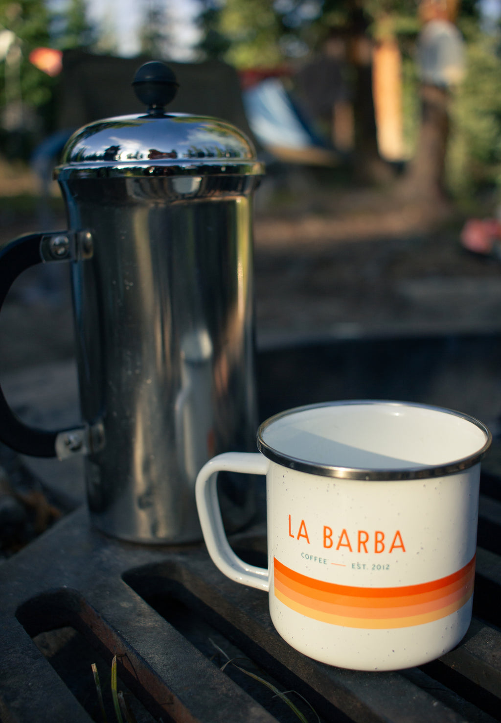 A white enamel mug with 'LA BARBA' printed in orange and red stripes on the side on a table