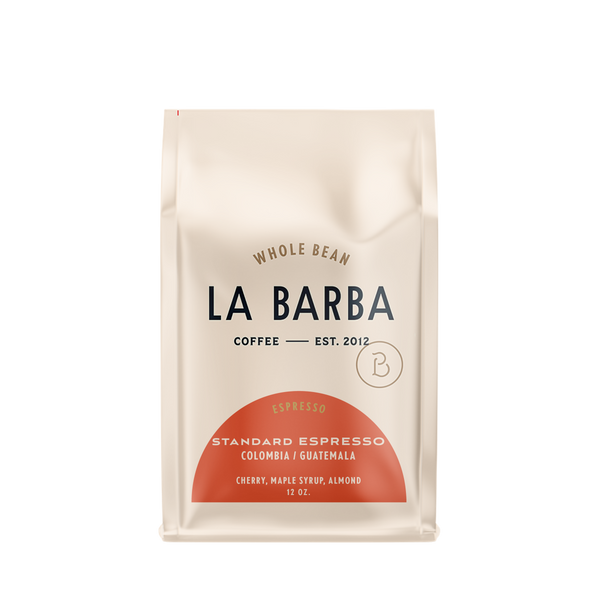 The image features a 12oz bag of La Barba Coffee, specifically their Standard Espresso Blend. The bag is designed with an ivory white background, prominently displaying the brand name "La Barba" in large, elegant letters. It highlights the coffee blend's origins, Colombia and Guatemala, and includes a description of the flavor profile, including notes of Cherry, Maple Syrup, and Almond. The design exudes a premium and modern feel with a minimalist, sophisticated look.