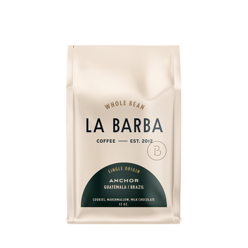 The image features a 12oz bag of La Barba Coffee, specifically their Anchor Blend. The bag is designed with an ivory white background, prominently displaying the brand name "La Barba" in large, elegant letters. It highlights the coffee blend's origins, Guatemala and Brazil, and includes a description of the flavor profile, including notes of Cookies, Marshmallow, and Milk Chocolate. The design exudes a premium and modern feel with a minimalist, sophisticated look.
