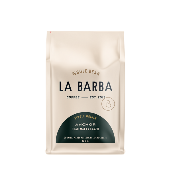 The image features a 12oz bag of La Barba Coffee, specifically their Anchor Blend. The bag is designed with an ivory white background, prominently displaying the brand name "La Barba" in large, elegant letters. It highlights the coffee blend's origins, Guatemala and Brazil, and includes a description of the flavor profile, including notes of Cookies, Marshmallow, and Milk Chocolate. The design exudes a premium and modern feel with a minimalist, sophisticated look.