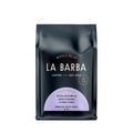 The image features a 12oz bag of La Barba Coffee, specifically their Colombia Andres Martinez Caturra Floral. The bag is designed with a dark background, prominently displaying the brand name "La Barba" in large, elegant letters. It highlights the coffee's origin, Colombia, along with a description of the flavor profile, including notes of london fog, papaya, and vanilla. The design exudes a premium and modern feel with a minimalist, sophisticated look.