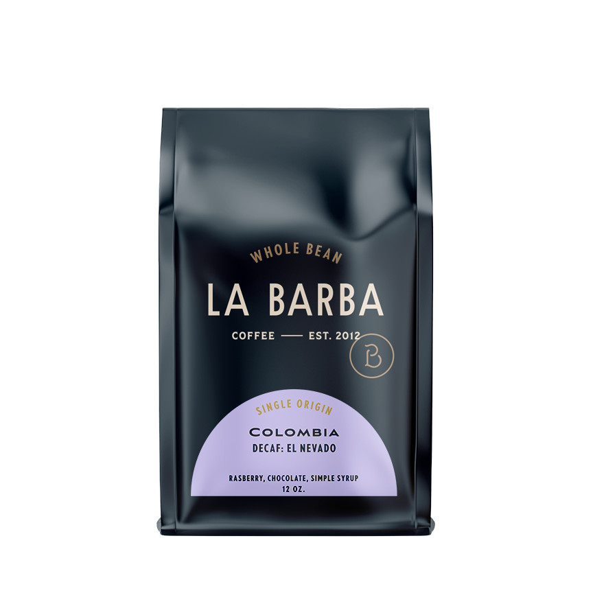 A dark navy La Barba Coffee bag standing upright on a white background. The packaging features minimalist, modern branding with cream-colored text reading ‘LA BARBA Coffee Est. 2012.’ A soft lavender label on the lower half highlights the single-origin Colombia Decaf: El Nevado coffee, with tasting notes of raspberry, chocolate, and simple syrup. The bag is sleek, glossy, and premium in appearance, designed for whole-bean coffee in a 12 oz size.