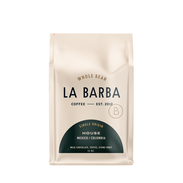 The image features a 12oz bag of La Barba Coffee, specifically their House Blend. The bag is designed with an ivory white background, prominently displaying the brand name "La Barba" in large, elegant letters. It highlights the coffee blend's origins, Mexico and Colombia, and includes a description of the flavor profile, including notes of Milk Chocolate, Toffee, and Stone Fruit. The design exudes a premium and modern feel with a minimalist, sophisticated look.