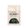 The image features a 12oz bag of La Barba Coffee, specifically their Noche Oscura Blend. The bag is designed with an ivory white background, prominently displaying the brand name "La Barba" in large, elegant letters. It highlights the coffee blend's origins, Ethiopia and Guatemala, and includes a description of the flavor profile, including notes of Chocolate, Marzipan, and Apple Butter. The design exudes a premium and modern feel with a minimalist, sophisticated look.