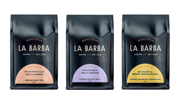 A set of three La Barba Coffee single-origin whole bean bags displayed side by side against a white background. Each bag features La Barba’s signature dark navy packaging with minimalist cream typography. The left bag highlights Guatemala Finca La Colmenita with flavor notes of chocolate, honey, and plum, showcased on a soft peach label. The middle bag features Colombia Finca La Concepcion with blackberry, cantaloupe, and vanilla notes on a light lavender label. The right bag presents Ethiopia Mulugeta Munt