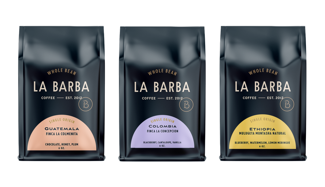 A set of three La Barba Coffee single-origin whole bean bags displayed side by side against a white background. Each bag features La Barba’s signature dark navy packaging with minimalist cream typography. The left bag highlights Guatemala Finca La Colmenita with flavor notes of chocolate, honey, and plum, showcased on a soft peach label. The middle bag features Colombia Finca La Concepcion with blackberry, cantaloupe, and vanilla notes on a light lavender label. The right bag presents Ethiopia Mulugeta Munt