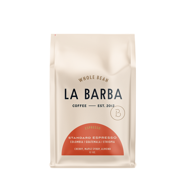 A 12 oz bag of La Barba Whole Bean Coffee, Standard Espresso, in a cream-colored stand-up pouch with a terracotta-colored semi-circle graphic at the bottom and black text.